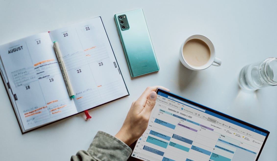 bird's eye view of a tablet with a calendar, a cup of coffee, and a planner.